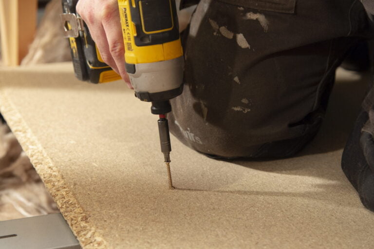 A screw being drilled into a floor board with an electronic drill.